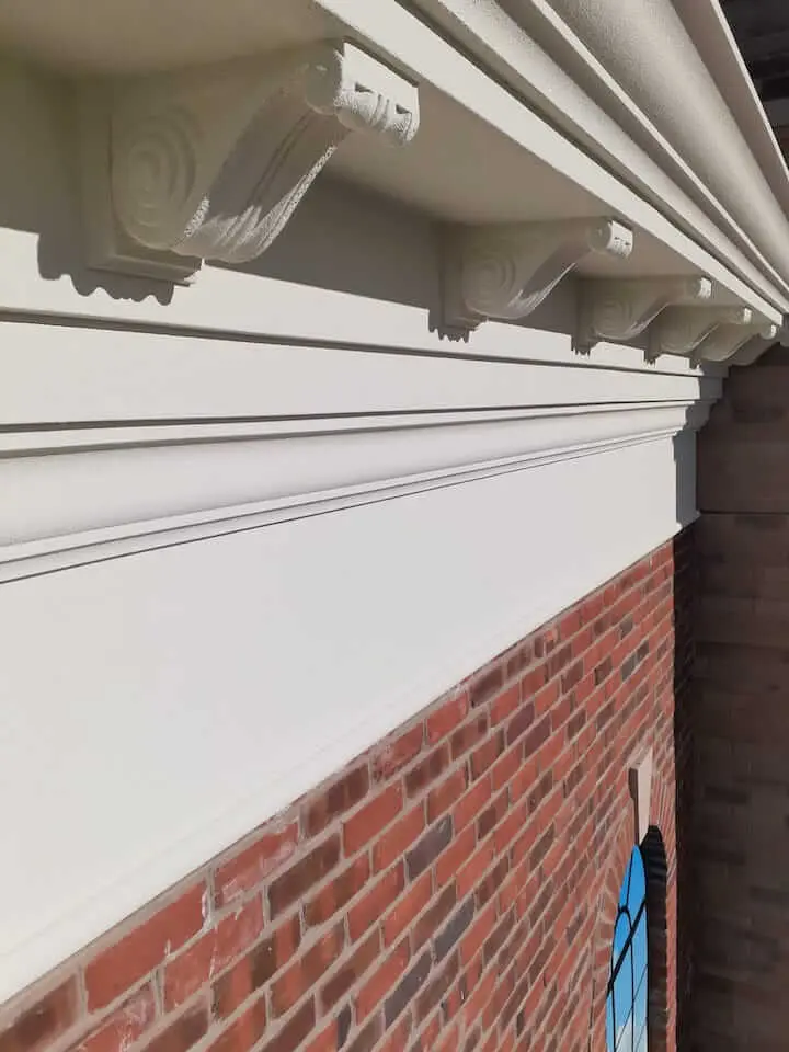 Exterior trim and soffit work in Toronto: aluminum and vinyl components each carry their own prep and temperature rules, separate from the body of the house Freshly painted white cornice, dentil moulding, and soffit against red brick on a Toronto home